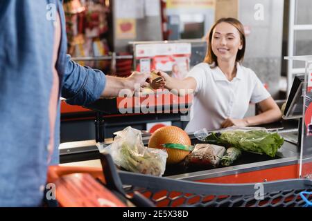 Uomo che dà carta di credito al cassiere sorridente vicino al cibo su checkout supermercato Foto Stock