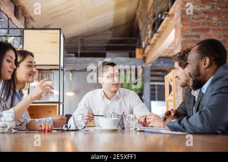 Colloqui. Gruppo diversificato di collaboratori che hanno una discussione informale in ufficio. Dirigenti durante discussioni amichevoli, rapporti mensili, incontri creativi. Concetto di business, finanza, occupazione, lavoro. Foto Stock