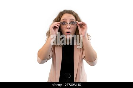 Giovane donna sorprende che tiene i suoi occhiali con le mani. Indossa una tuta di colore corallo, isolata su sfondo bianco. Foto Stock