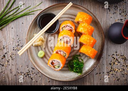 Sushi maki Rolls California Futomaki con salmone, avocado, cetriolo, granchio e uova di pesce volante su un piatto con chopsticks, salsa di soia, wasabi e zenzero Foto Stock