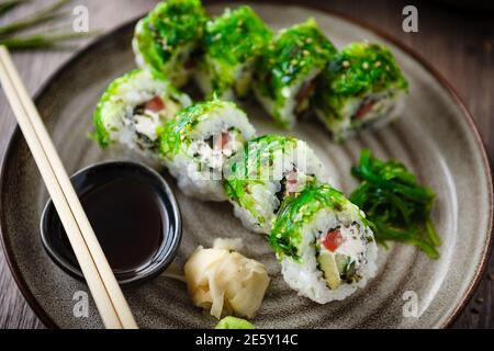 Panini di sushi maki con cetriolo, avocado, pomodoro, formaggio cremoso, chuka wakame su un piatto con chopsticks, salsa di soia, wasabi e zenzero. Giapponese Foto Stock