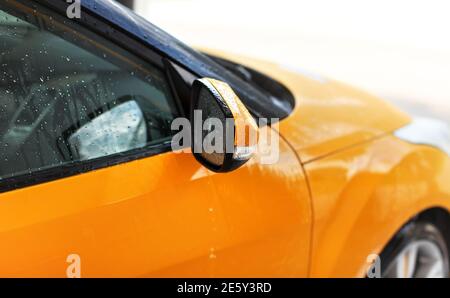 Auto gialla arancione lavata in autolavaggio, dettaglio su specchio laterale con gocce d'acqua Foto Stock