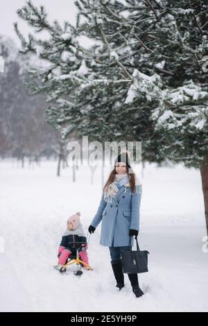 Bambina che si diverge a sledding. Mamma che slitta la sua piccola figlia. Vacanze in famiglia nella vigilia di Natale all'aperto Foto Stock