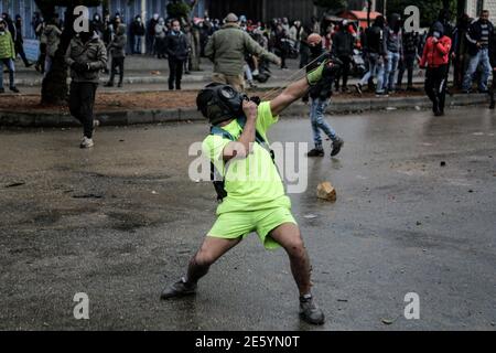 Tripoli, Libano. 28 Gennaio 2021. Un attivista anti-governo fa precipitarsi le rocce con un colpo di schiaffo contro la polizia antisommossa nei pressi di Serail (sede del Governatorato) durante una protesta contro le cattive situazioni economiche che il paese si trova ad affrontare in mezzo a un blocco nazionale del coronavirus per frenare la diffusione della pandemia del coronavirus. Un uomo ha perso la vita e almeno 200 persone sono rimaste ferite negli ultimi due giorni a causa delle manifestazioni in corso. Credit: Marwan Naamani/dpa/Alamy Live News Foto Stock