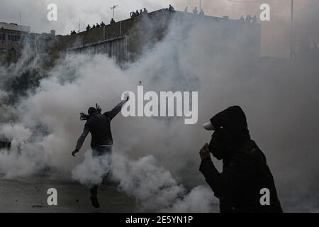 Tripoli, Libano. 28 Gennaio 2021. Un attivista anti-governativo lancia pietre contro la polizia antisommossa che protegge Serail (sede del Governatorato) durante una protesta contro le cattive situazioni economiche che il paese deve affrontare in mezzo a un blocco nazionale del coronavirus per frenare la diffusione della pandemia del coronavirus. Un uomo ha perso la vita e almeno 200 persone sono rimaste ferite negli ultimi due giorni a causa delle manifestazioni in corso. Credit: Marwan Naamani/dpa/Alamy Live News Foto Stock