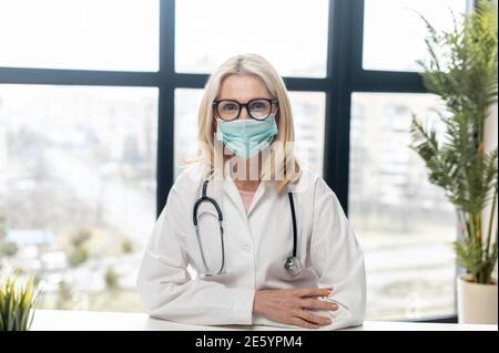 Ritratto in primo piano di una donna sicura MD, medico, terapeuta, pediatrica in maschera protettiva in piedi con le braccia incrociate e guarda la fotocamera in Foto Stock
