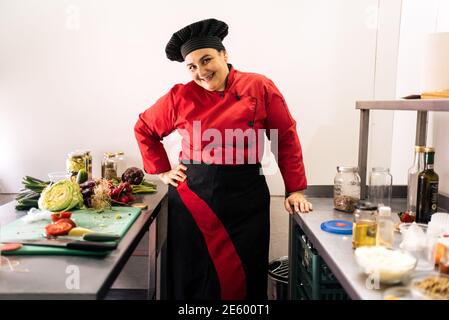 Foto di borsa di donna che lavora in cucina del ristorante indossando grembiule e cappello da cucina. Foto Stock