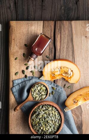 Olio di semi di zucca pressato a freddo in una bottiglia di vetro, decorato con semi sbucciati su un tavolo di legno Foto Stock