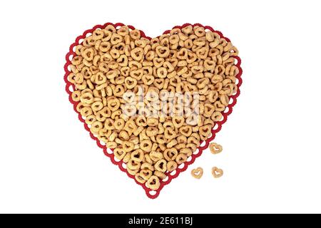 primo piano di cereali per la colazione con cerchi e cuori su rosso merletto cuore isolato doily su bianco Foto Stock