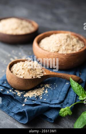 Supplemento dietetico, fiocchi di lievito nutritivi imprevisti in una ciotola di legno e paletta sullo sfondo di pietra Foto Stock