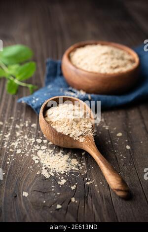Supplemento dietetico, fiocchi di lievito nutritivi imprevisti in una ciotola di legno e paletta su un tavolo di legno Foto Stock
