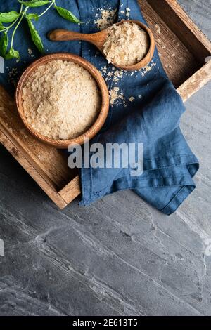 Supplemento dietetico, fiocchi di lievito nutritivi imprevisti in una ciotola di legno e paletta sullo sfondo di pietra con spazio di copia Foto Stock