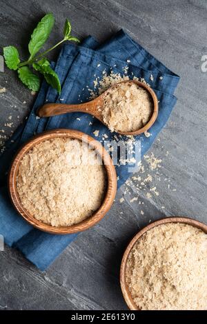 Supplemento dietetico, fiocchi di lievito nutritivi imprevisti in una ciotola di legno e paletta sullo sfondo di pietra Foto Stock