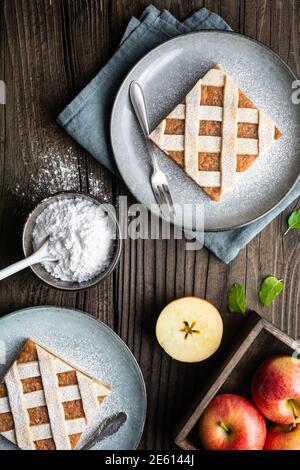 Fette di torta alla cannella di mele con cima a graticcio, cosparse di zucchero in polvere su vecchio fondo di legno Foto Stock