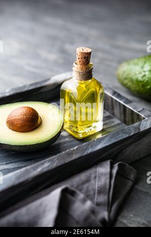 Olio di avocado sano in una bottiglia di vetro, decorato con avocado affettato su fondo di pietra Foto Stock