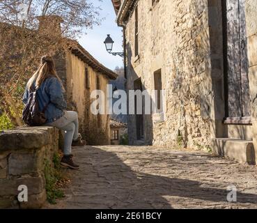 Giovane bella donna seduta su muro di roccia che guarda il paesaggio nella vecchia città medievale di Rupit, Barcellona, Spagna Foto Stock