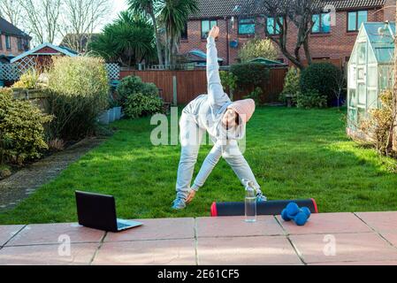 Donna che fa l'allenamento sportivo all'aperto nel suo giardino, cortile con tutorial online o allenatore. Stile di vita sano durante un blocco. Esercitarsi a casa Foto Stock