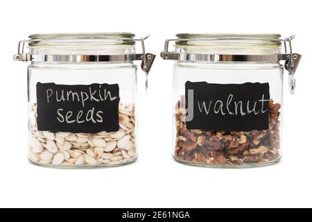 Semi di zucca e noci in vasetti di vetro, chiusura a scatto, isolati su sfondo bianco Foto Stock