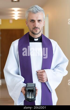 Nel corso di una visita pastorale, il lettore di carte è presente in un bel giovane sacerdote. Foto Stock