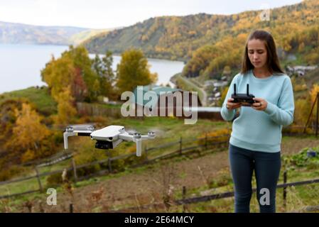 Figura sfocata di ragazza controlla un drone su sfondo sfocato autunno. Confetto messa a fuoco morbida Foto Stock