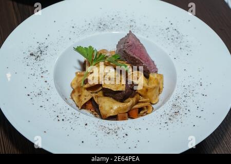 Pasta al forno con carne di selvaggina a fette condita con prezzemolo, servita su un piatto Foto Stock