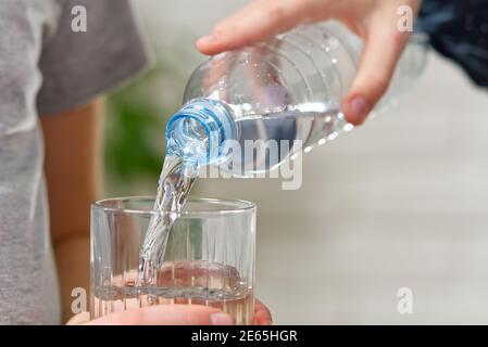 ragazzo versa acqua dalla bottiglia di plastica nel vetro su tavolo di legno Foto Stock