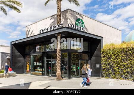 Un moderno edificio Starbucks Coffee con una palma che cresce la loro facciata e la gente che cammina. Foto Stock