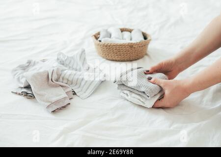 Donna che piega i vestiti in cesto di iuta nel sistema di konmari. Concetto di organizzazione di abiti minimalisti. Foto Stock