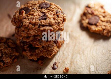 Accatastati biscotti appena fatti su carta da forno. Questi sono fatti con avena intera di grano arrotolata con i trucioli di cioccolato scuro. Ci sono pezzi e crumbles sopra Foto Stock