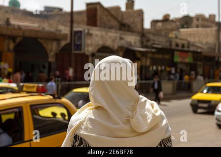 Un siriano che indossa abiti tradizionali locali è in piedi su una strada trafficata nel quartiere storico della città siriana settentrionale di Aleppo. Retro sfocato Foto Stock