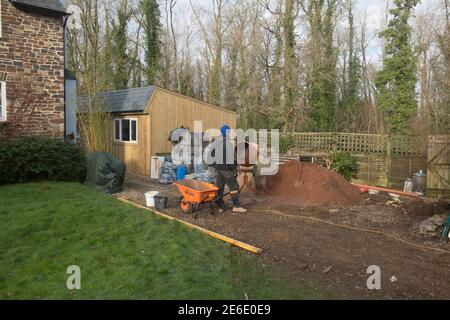 Operai o costruttori che mescolano calcestruzzo su un luogo di costruzione in un giardino rurale in Devon rurale, Inghilterra, Regno Unito Foto Stock