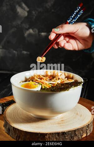 La giovane donna giapponese che cena assaggia il delizioso ramen dell'udon - zuppa giapponese di ramen con pollo, uovo, aglio e noodle su uno sfondo di legno scuro Foto Stock