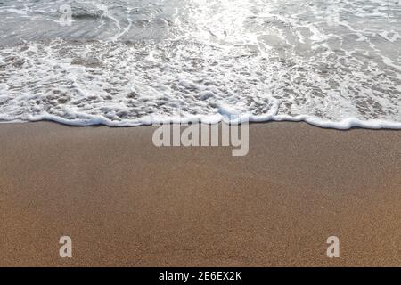 Le onde morbide dell'oceano blu sulla spiaggia sabbiosa, le bolle di schiuma di acqua, il periodo estivo di vacanza. Foto Stock