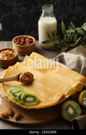 Concetto di colazione con crepes con kiwi, burro di arachidi e noci su sfondo grigio Foto Stock