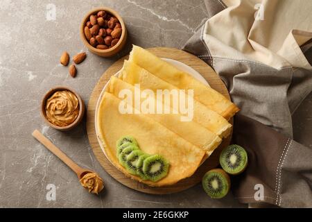 Concetto di colazione con crepes con kiwi, burro di arachidi e noci su sfondo grigio Foto Stock