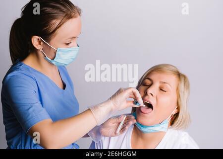 Foto ingrandita di un infermiere che prende un'analisi orale da una donna anziana su sfondo bianco. Foto Stock