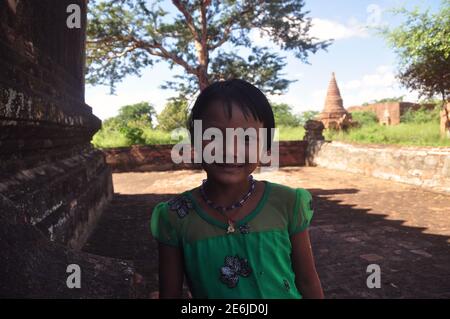 BAGAN, MYANMAR - 18 NOVEMBRE 2015 Ritratto di adorabile bambina etnica nel cortile di pietra della città tropicale guardando la macchina fotografica, Myanmar. Piccolo affascinante Foto Stock