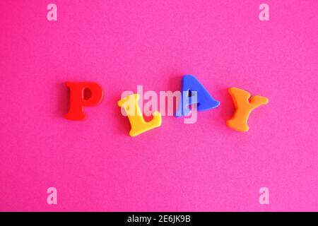 Gioca la parola in lettere magnetiche colorate di plastica su un rosa sfondo viola Foto Stock