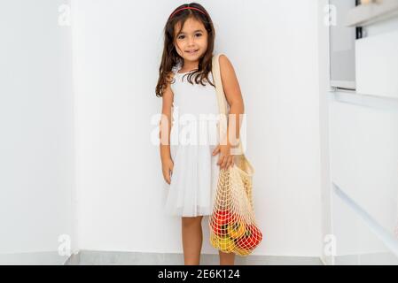 Bambino piccolo che tiene i sacchetti riutilizzabili della spesa della rete con le verdure e la frutta. Bella ragazza nera con eco-friendly mesh shopper. Zero sprechi, concetto di plastica, shopping senza sprechi. Foto Stock