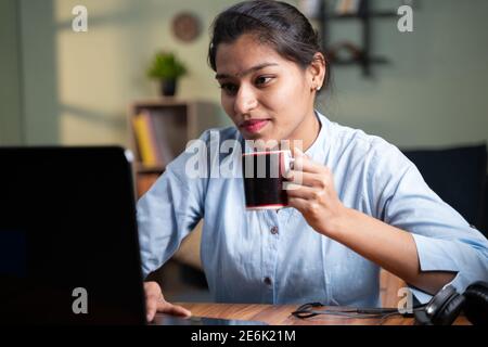 Giovane donna d'affari che ha il caffè mentre lavora su un computer portatile - concetto di prendere la pausa, rilassarsi o godersi il caffè durante il lavoro Foto Stock