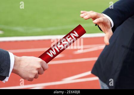 Uomini d'affari che passano il testimone in gara di relè con la parola tedesca Wissen Significa conoscenza Foto Stock