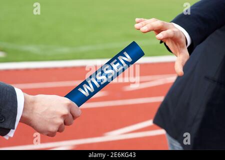 Uomini d'affari che passano il testimone in gara di relè con la parola tedesca Wissen Significa conoscenza Foto Stock