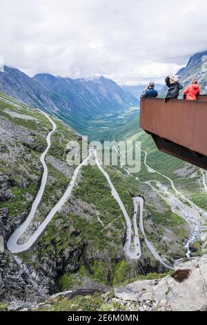 I turisti sul punto panoramico Trolls Point ammirando la montagna Trollstigen passa e il bellissimo paesaggio sotto e intorno a loro - Viaggiare in Norvegia Foto Stock