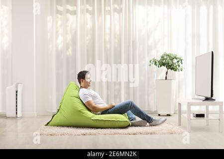 Profilo di un giovane uomo casual seduto su un poltrona con sacco di fagioli verdi e guardare la tv a casa Foto Stock