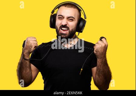 Uomo hipster con le cuffie che si aggirano intorno a filo di strappo sfondo isolato giallo Foto Stock