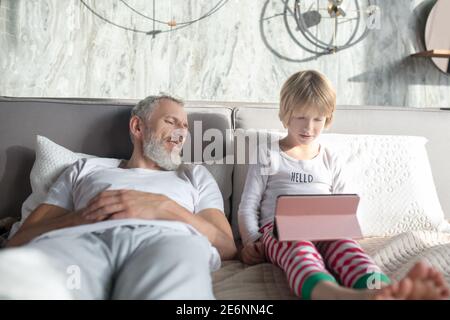 Uomo che giace bambino con tablet seduto sul letto Foto Stock