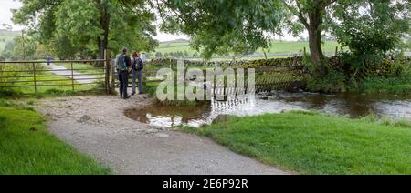 Camminatori che attraversano un cancello su un sentiero che corre accanto A Malham Beck nelle valli dello Yorkshire Foto Stock