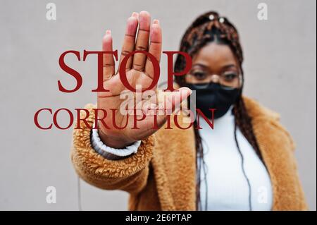 Fermare la corruzione. Donna afroamericana, indossare maschera nera mostra segno di stop mano. Foto Stock
