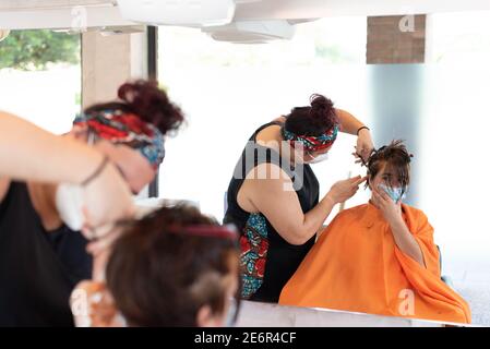 Lavorando durante il covid-19 o il concetto di coronavirus. Un parrucchiere professionista che taglia i capelli ad un cliente. Riflessione nello specchio. Foto Stock