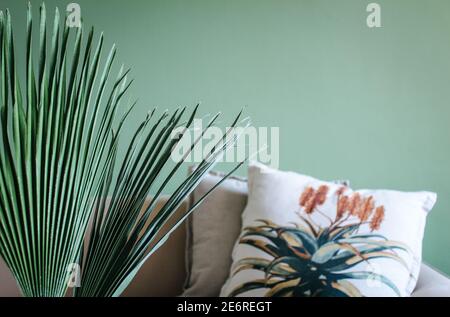 Divano beige vintage con un cuscino con stampa floreale di piante in piedi davanti a una parete verde. Foto Stock